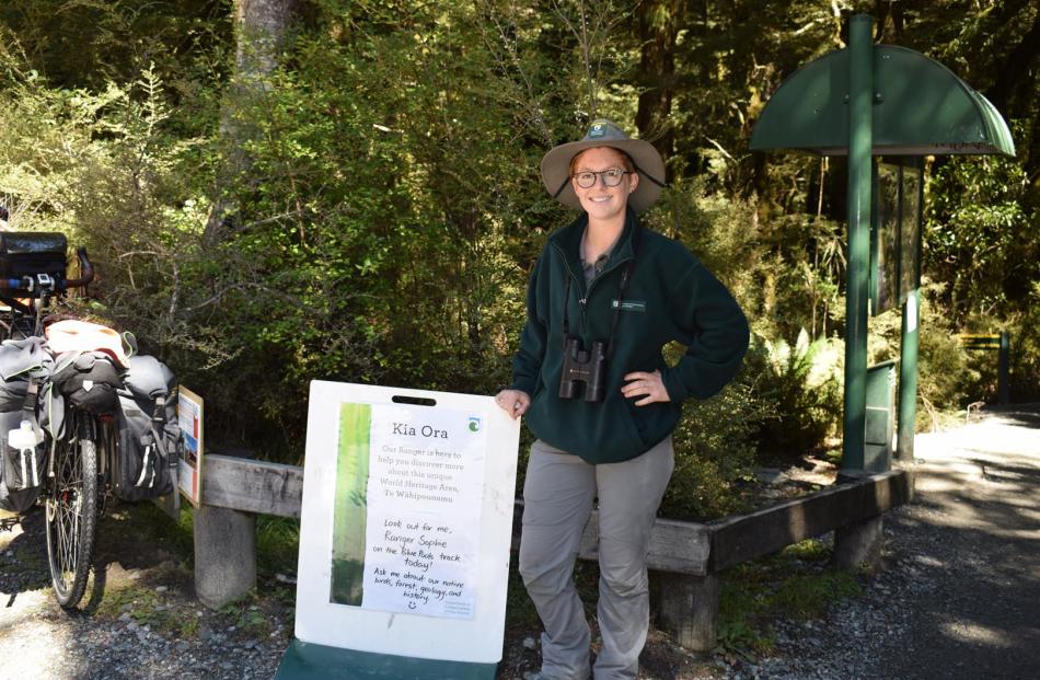 Ranger Sophie Briggs standing beside the Doc notice at the start of the Blue Pools Track alerting walkers there is a ranger on the walk today. Photos: Kerrie Waterworth
