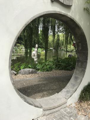 A moon gate forms a circular frame for a garden view. 
