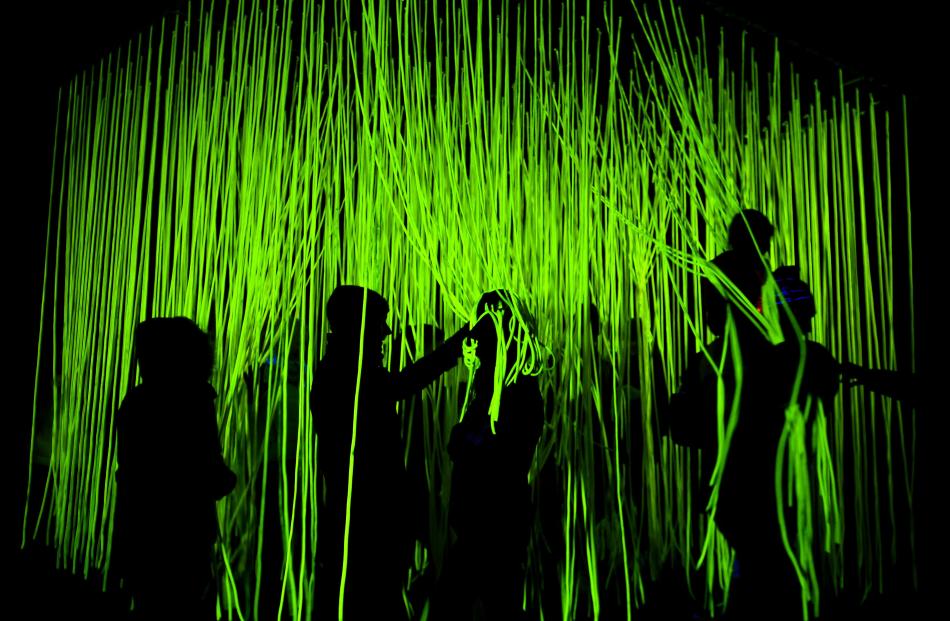 People walk through a glowing forest of rope called UV Spaghetti at the Luma opening night.