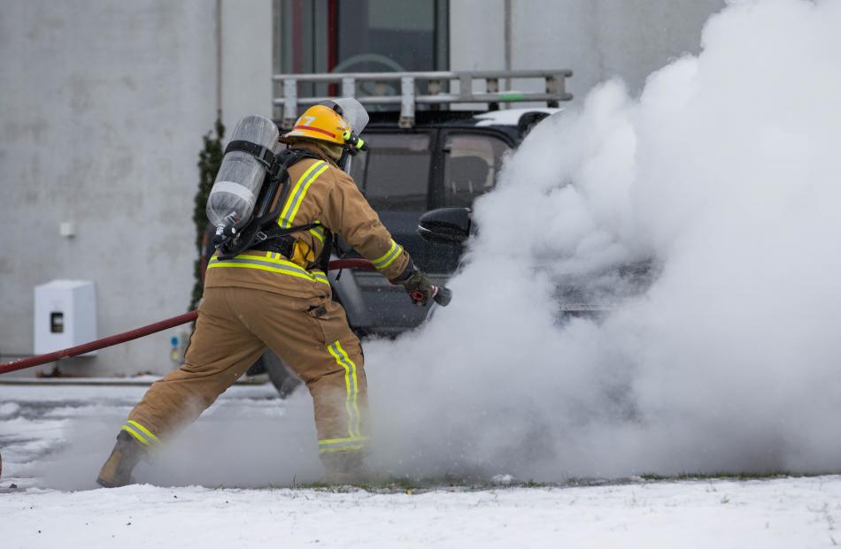 A firefighter extinguishes the car on fire at a Queenstown dealership yesterday. Photos: James Allan