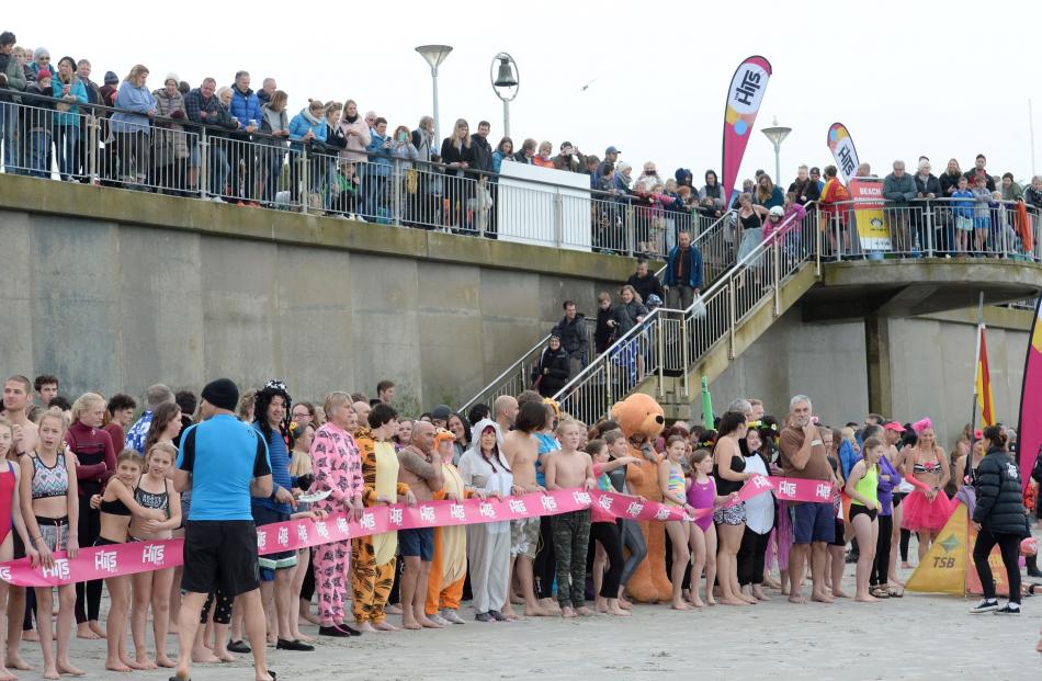 Spectators on the Esplanade keep warm while, below, those taking part in the Polar Plunge try to...