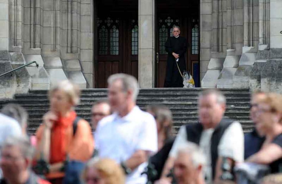 The Reverend Father Geoff Hughes and his hearing ear dog Toby watch from the steps of St Paul's...