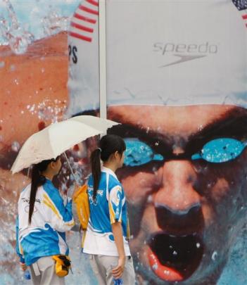 Olympic volunteers walk past a giant poster outside the National stadium at the Beijing 2008...