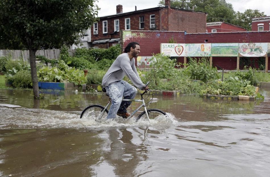 A man tries to ride a bicycle as floodwaters, covered in leaking kerosene, fill a neighbourhood...