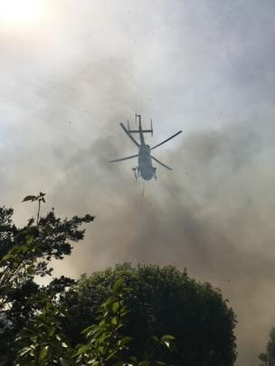 A rescue helicopter, obscured by smoke, fights the blaze with a monsoon bucket. Photo: Supplied