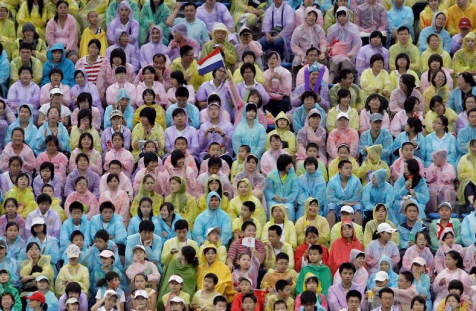 Fans all wearing pastel-colored rain ponchos watch a softball game between Japan and Netherlands....