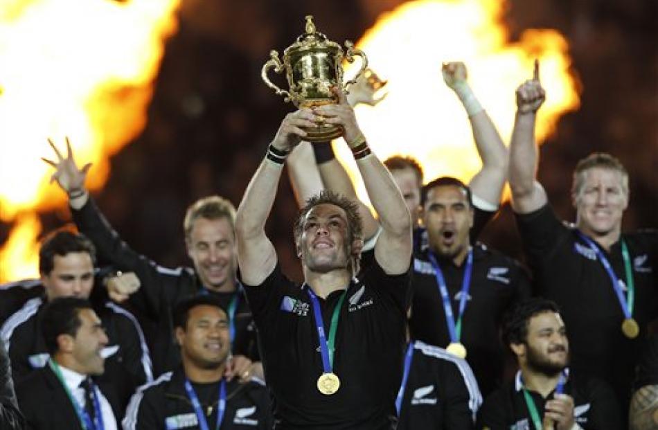 Richie McCaw holds up the Webb Ellis trophy as teammates celebrate. (AP Photo/Christophe Ena)