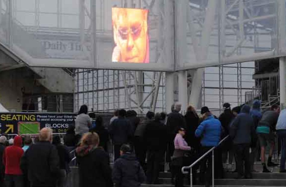 Those without tickets watch the screen through a gap between the stands.