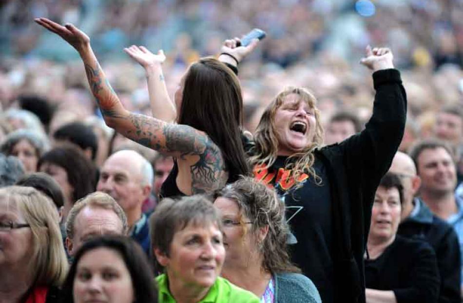 Two fans in the 35,500-strong crowd take to their feet as Sir Elton performs.