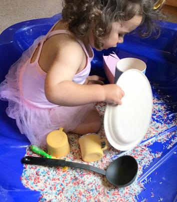 Madeline Gallagher (nearly 2) plays in the lounge with dyed rice, plates, cups and spoons....