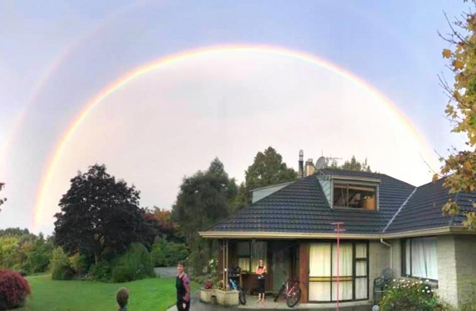 A rainbow arcs over Bree (12), Brony and Libby (10) Campbell as they shelter in their balcony on...