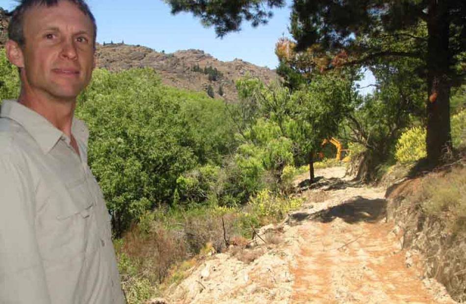 Mr Dennis stands on the trail while contractors work in the background to clear vegetation.