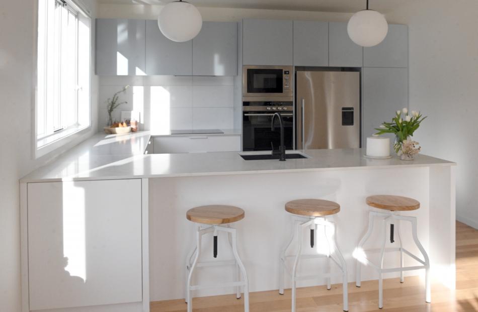 Pale blue cabinets provide soft colour in the otherwise white kitchen. Bifold windows over the...