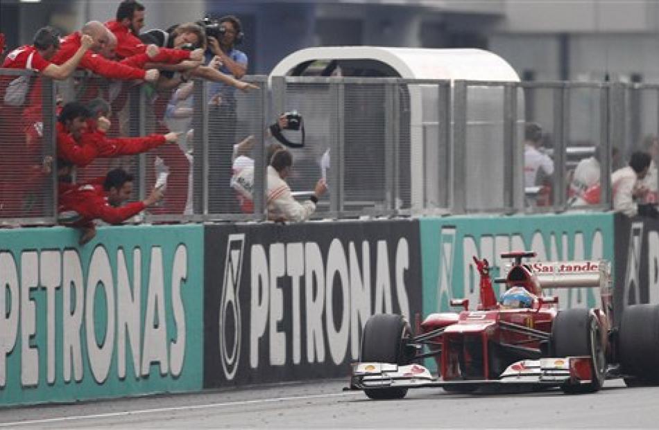 Ferrari driver Fernando Alonso of Spain celebrates as he passes his team on the pit lane wall...
