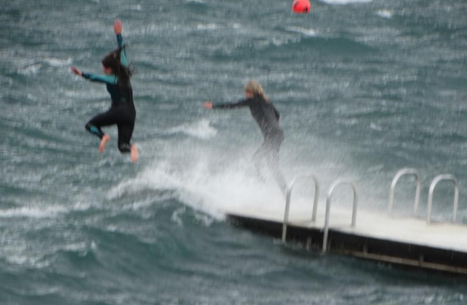 Young people leap from the swimming pontoon into the choppy waters of Lake Wanaka at Roys Bay...