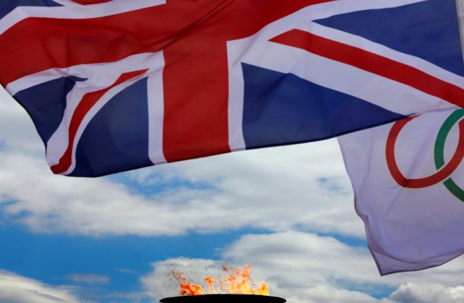 A British flag flutters next to a cauldron with the Olympic Flame atop the Acropolis in Athens...