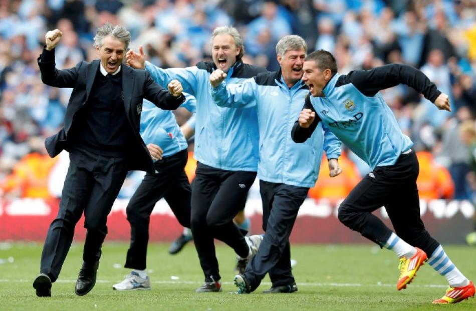 Manager Roberto Mancini (L) runs on to the pitch after Manchester City  won their English Premier...