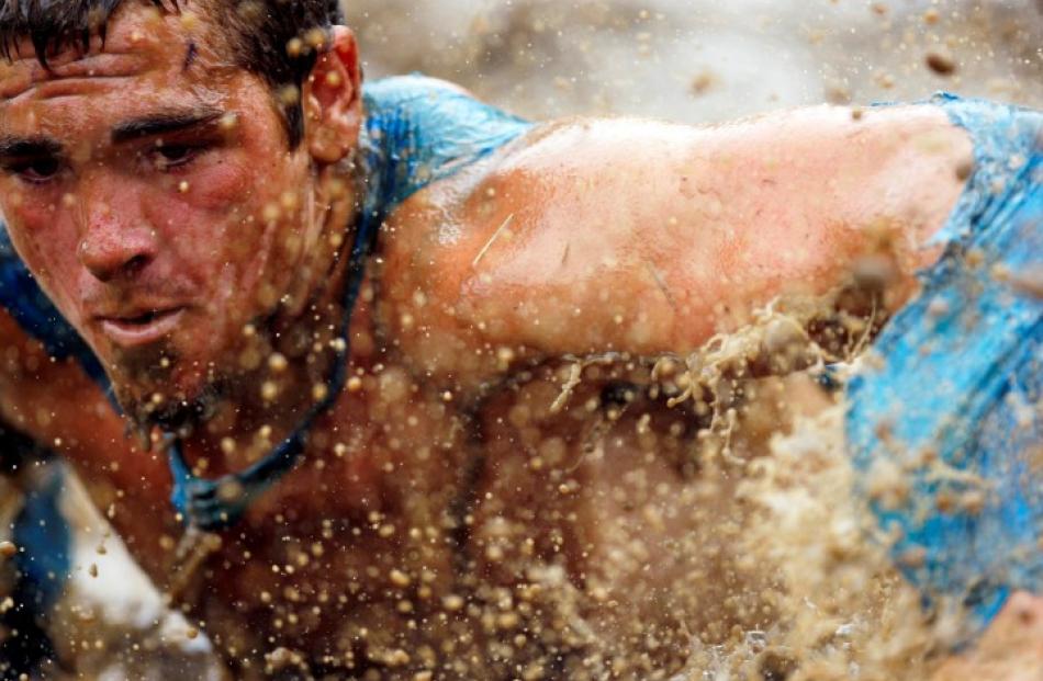 A competitor swims through mud underneath electrified wires during the Tough Mudder at Mt. Snow...