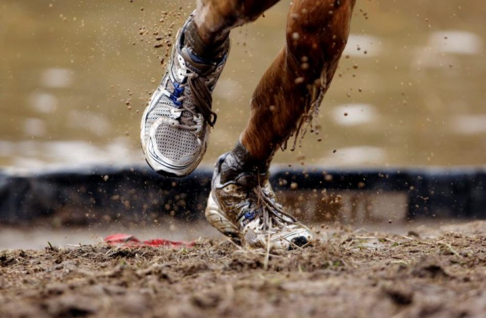 Mud flies off a competitor's shoes as he runs out of an obstacle during the Tough Mudder. REUTERS...