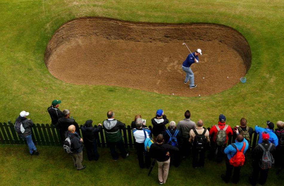 Spectators watch English golfer Justin Rose hit out of a bunker during a practice round for the...