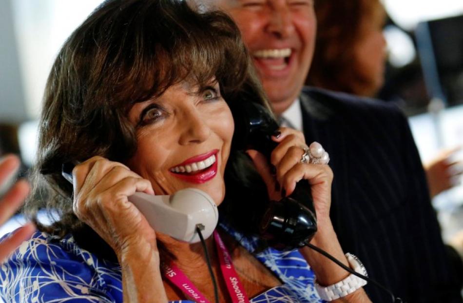 Actress Joan Collins speaks on a telephone as she takes part in a charity event on the trading...