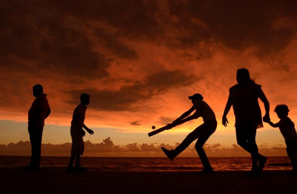 People play cricket as people walk along the seafront at Galle face green in Colombo before the...