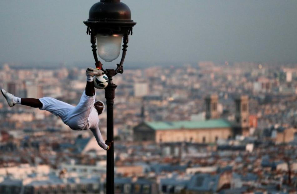 A football freestyler performs on a light pole next to the Sacre Coeur Basilica in Paris. REUTERS...