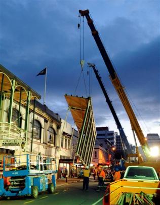 Cranes combine to remove part of the Harvest Court Mall facade on Tuesday night.