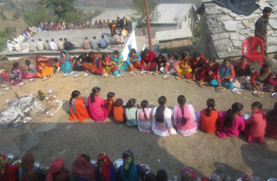 Women in bright saris sit separate from the men during a meal to mark a Hindu festival in the...