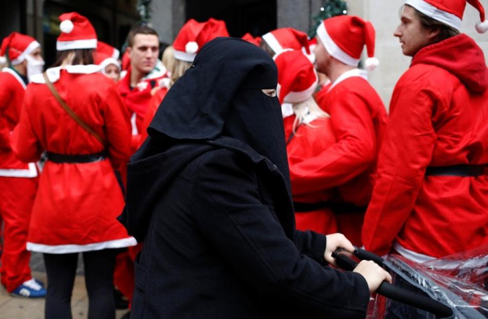 A woman wearing a niqab passes a group of people dressed as Father Christmas on a Santa-themed...