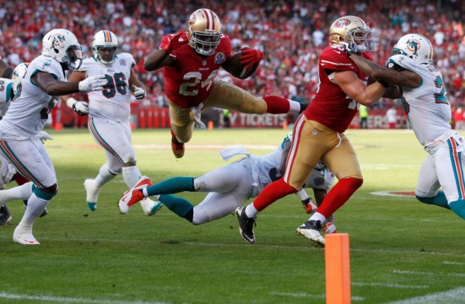 San Francisco 49ers running back Anthony Dixon (C) leaps over Miami Dolphins defenders to take...