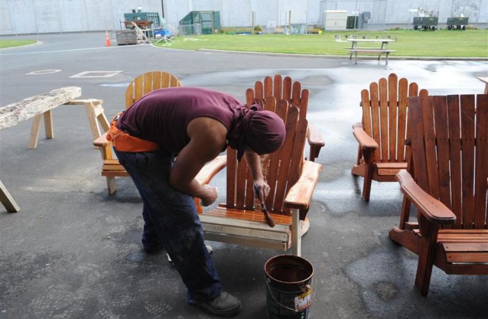 A prisoner stains outdoor chairs.