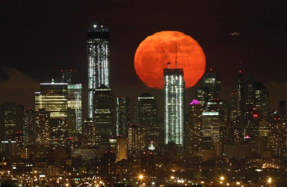 A full moon rises over the skyline of Lower Manhattan and One World Trade Center (L) in New York...