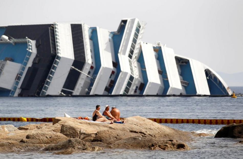 Vacationers bask in front of the wreckage of capsized cruise liner Costa Concordia near the...