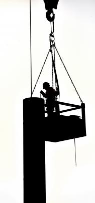 A worker is silhouetted against a cloudy sky as he is lifted by crane to the top of one of the...