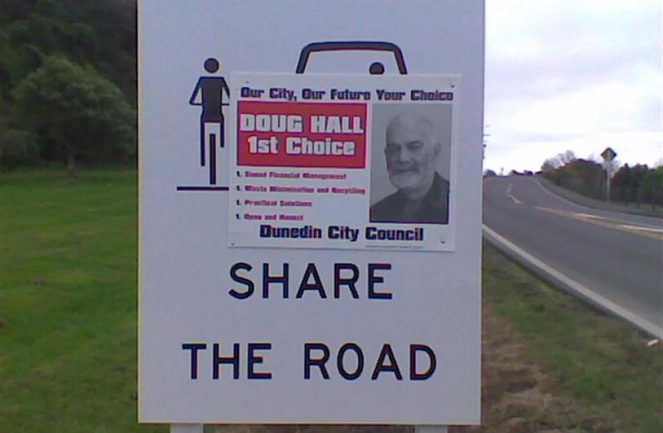 A stolen Doug Hall campaign poster shares space on a 'share the road' sign beside State Highway...