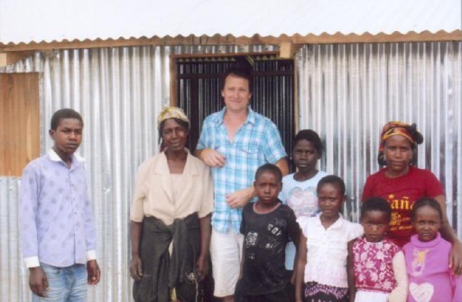 Paul Rogers (centre) stands with a Kenyan family in front of their new home in the Internally...