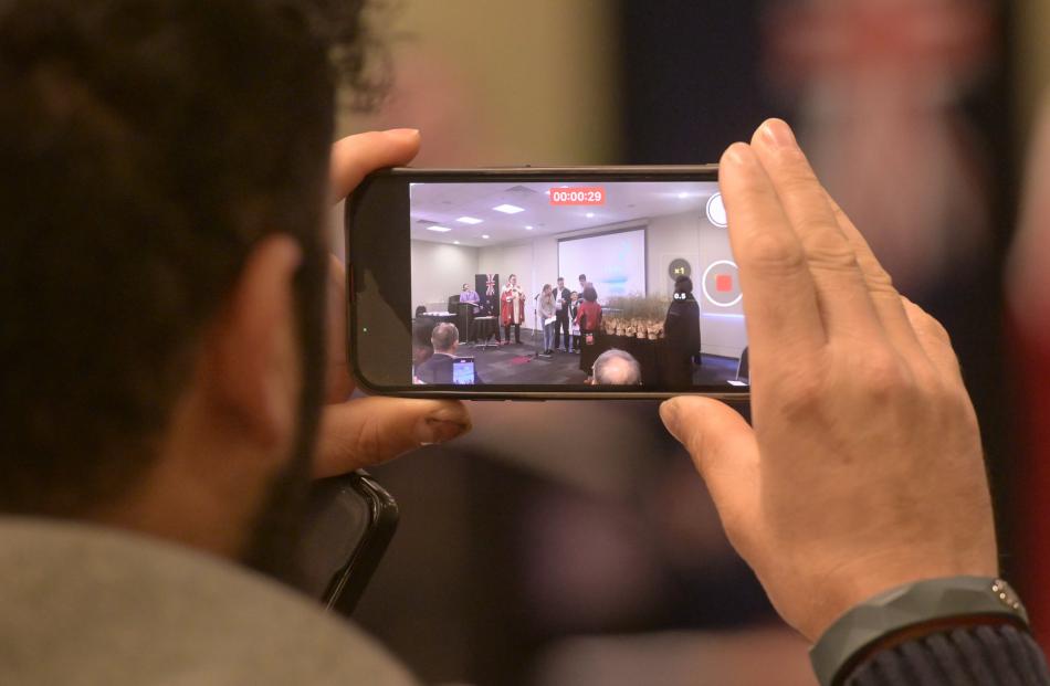 A man records part of the citizenship ceremony.