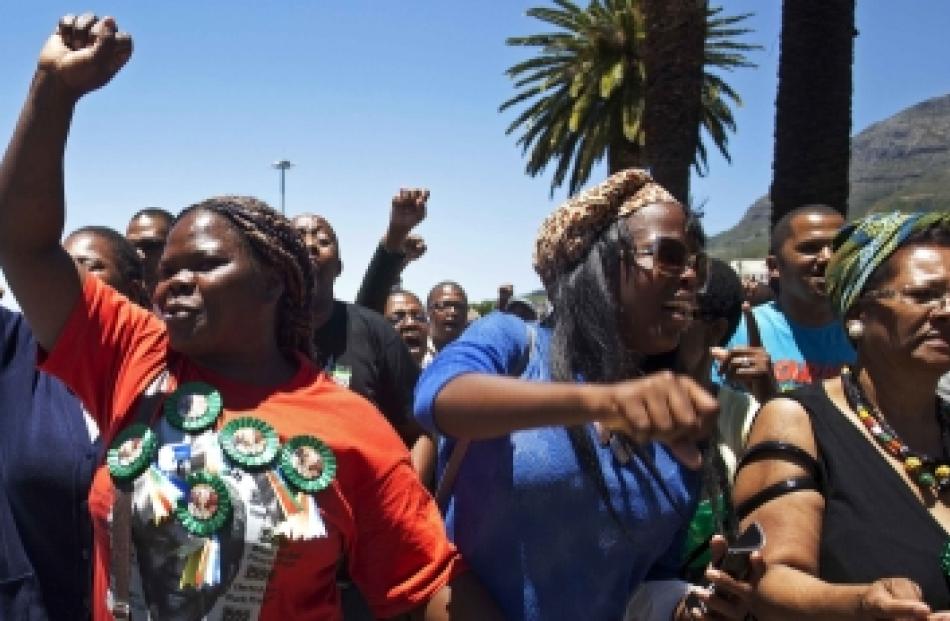 A woman with a Nelson Mandela t-shirt and badges sings and dances along with others in front of...