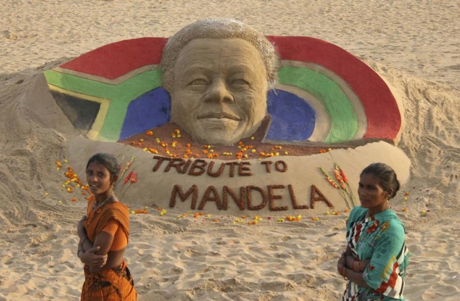 Women walk past a sand sculpture paying tribute to former South African President Nelson Mandela...