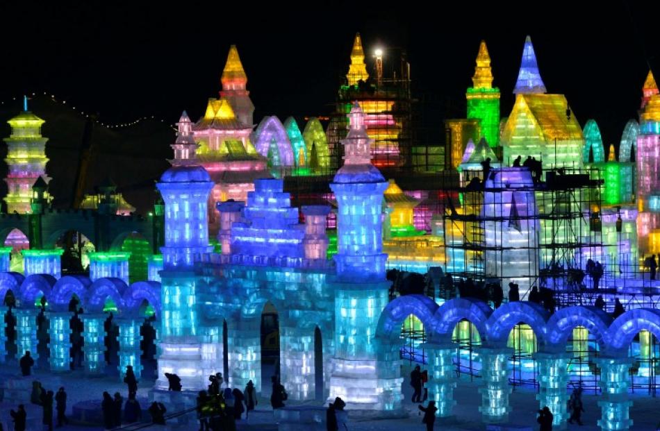Workers and scaffoldings are seen next to newly-built ice sculptures illuminated by coloured...