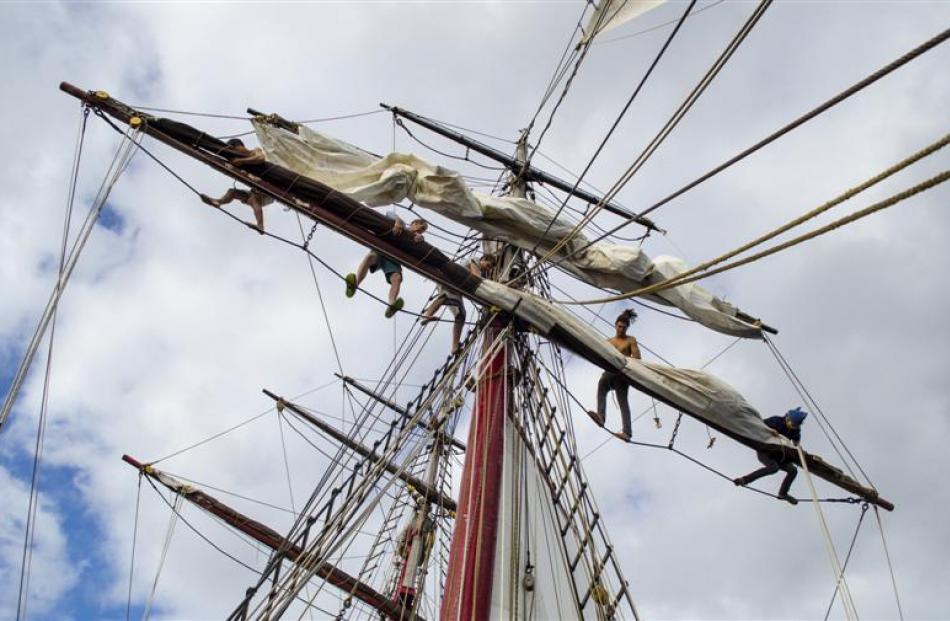 The crew aloft furl the fore square sails.