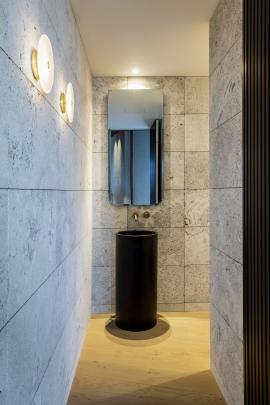 The powder room has a freestanding black, concrete basin with a brass tap, mixer and hidden towel...