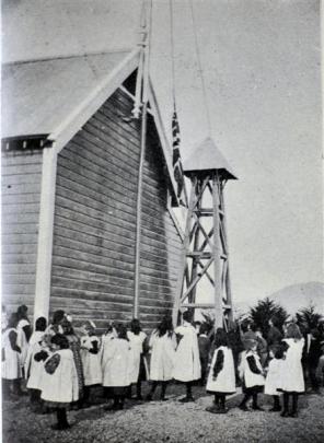 Wylies Crossing School pupils hoist the flag at an earlier building. Photo from Otago Witness,...