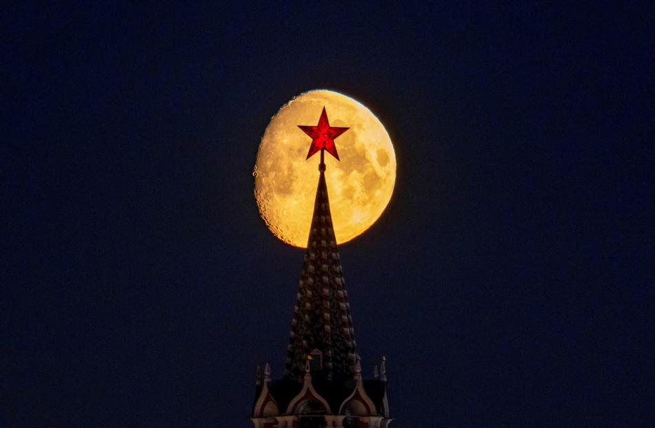 The moon rises behind the Kremlin’s Spasskaya Tower and the red star on its top, in central...