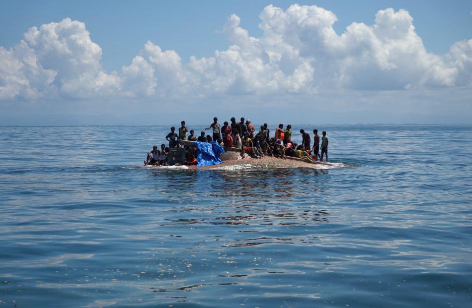 Rohingya refugees wait on a capsized boat before being rescued in the waters of West Aceh,...