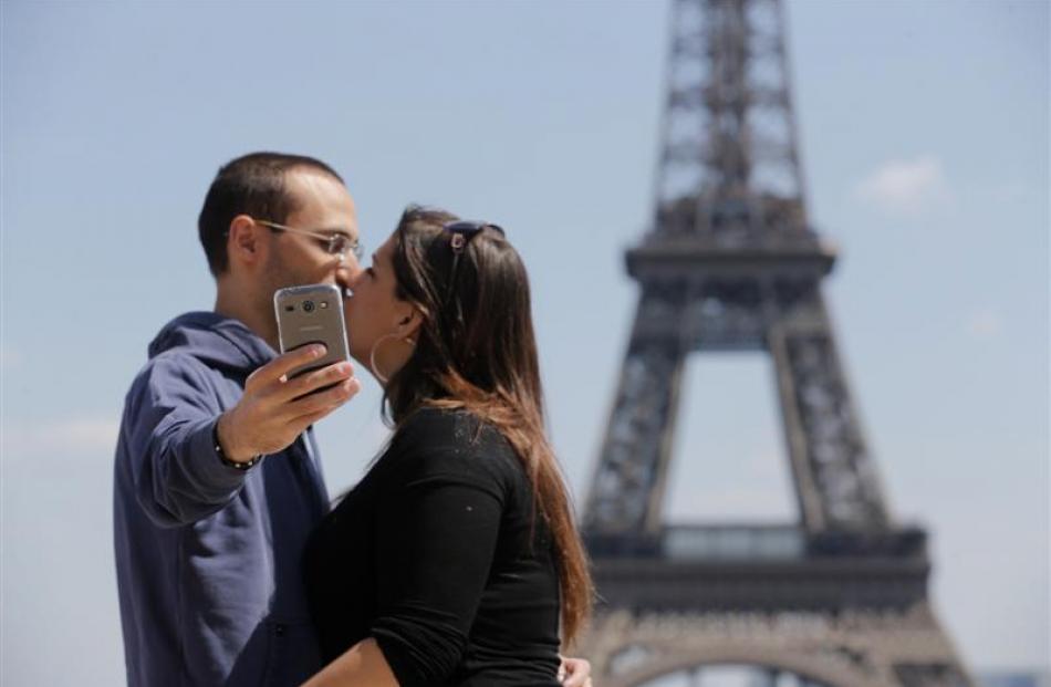 A couple of tourists use a mobile phone to take a selfie picture as they kiss at the Trocadero...