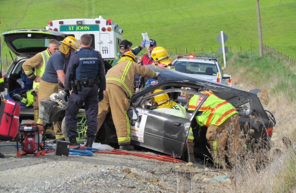 Trapped . . . Rescuers work on freeing the driver of the crashed car while paramedics provide...