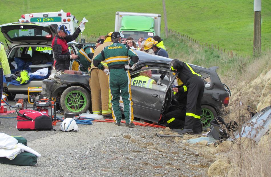 Trapped . . . Rescuers work on freeing the driver of the crashed car while paramedics provide...