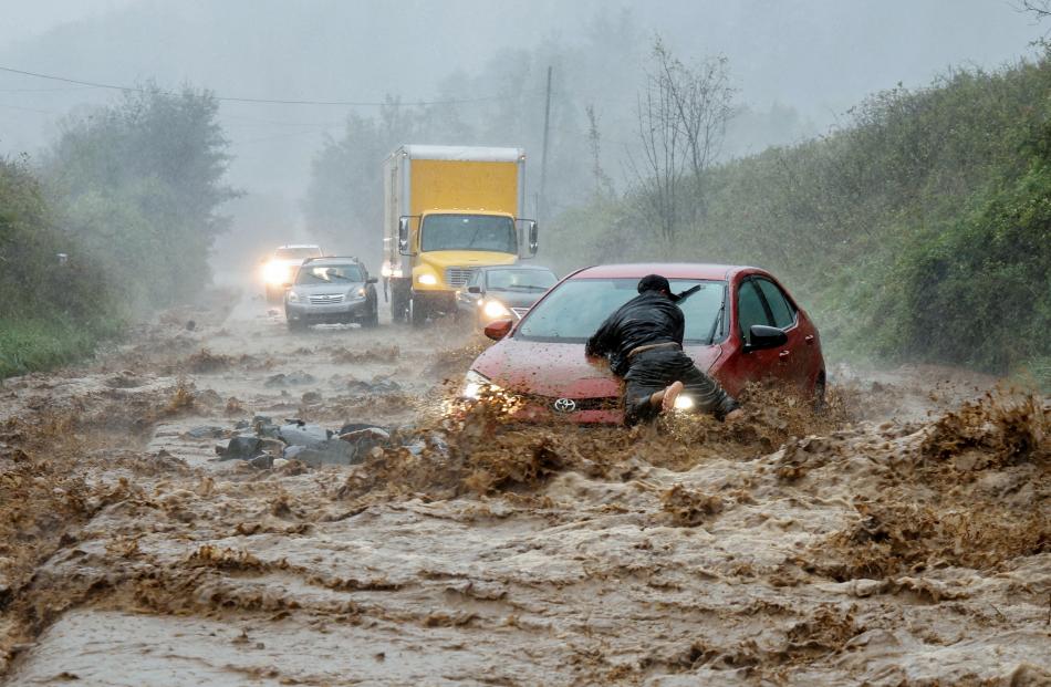 A local resident helps free a car that became stranded in a stretch of flooded road as Tropical...